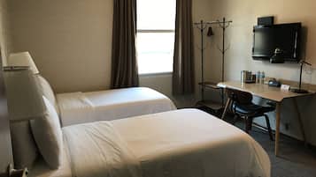 Habitación de hotel con dos camas, un escritorio, una silla, un televisor y un perchero.