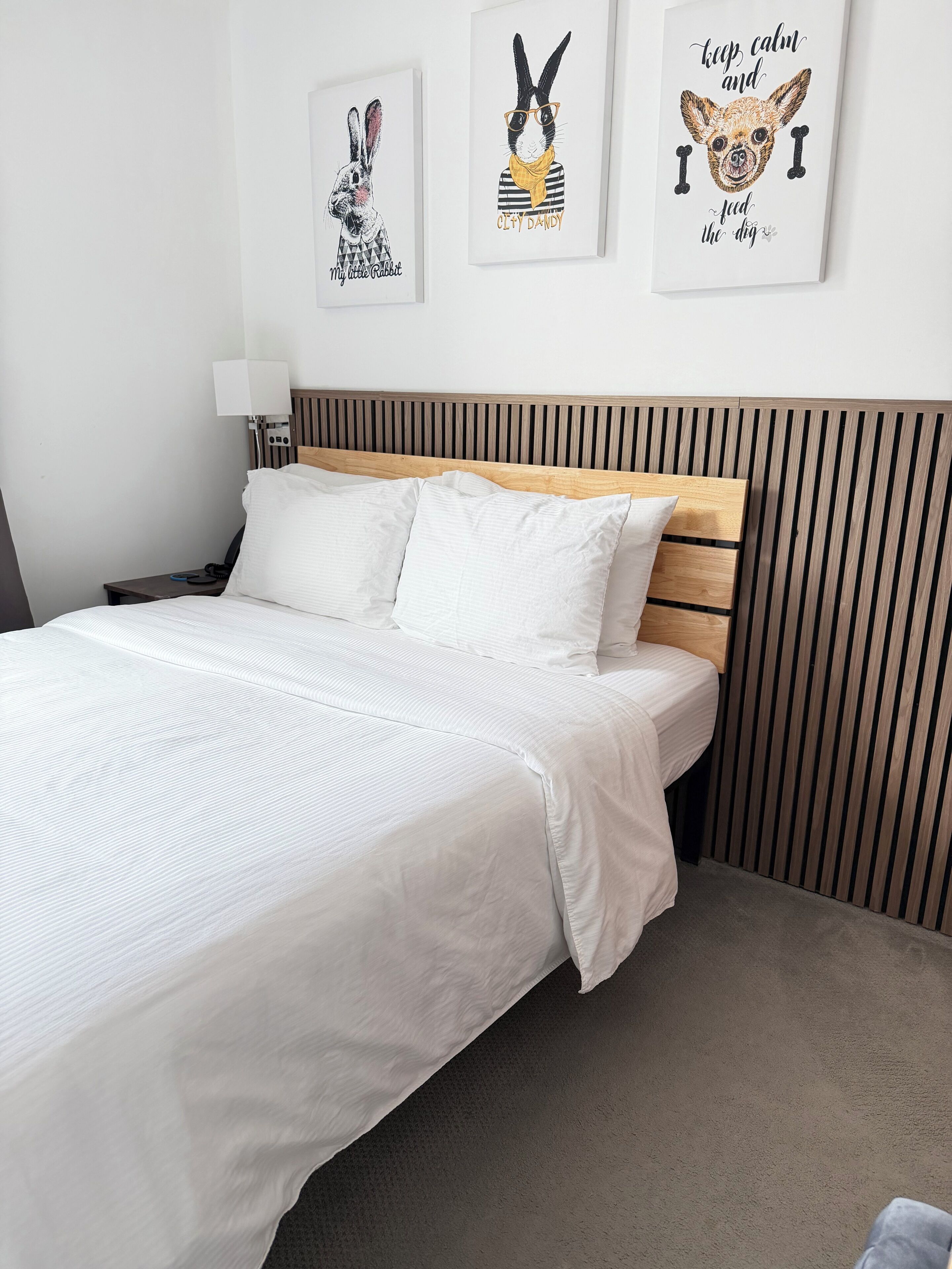 Una cama bien hecha con sábanas blancas, un cabecero de madera y dos obras de arte enmarcadas en la pared.