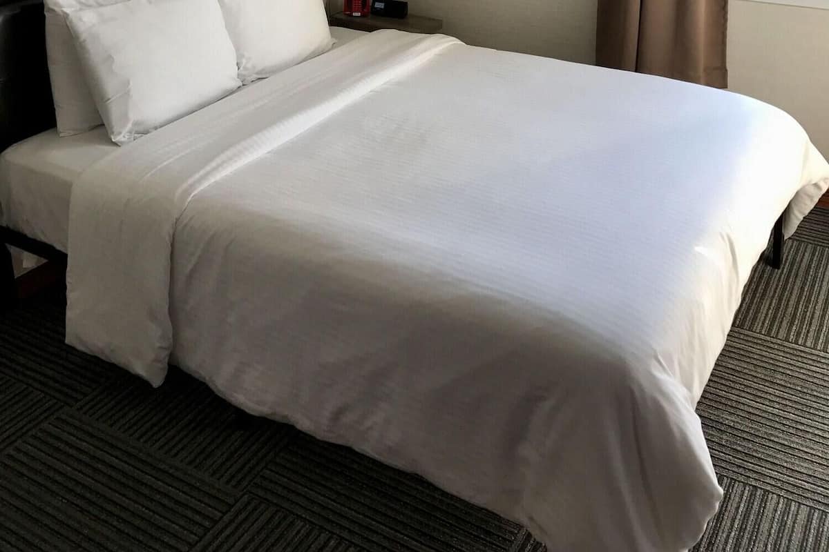 A neatly made bed with white linens in a hotel room.