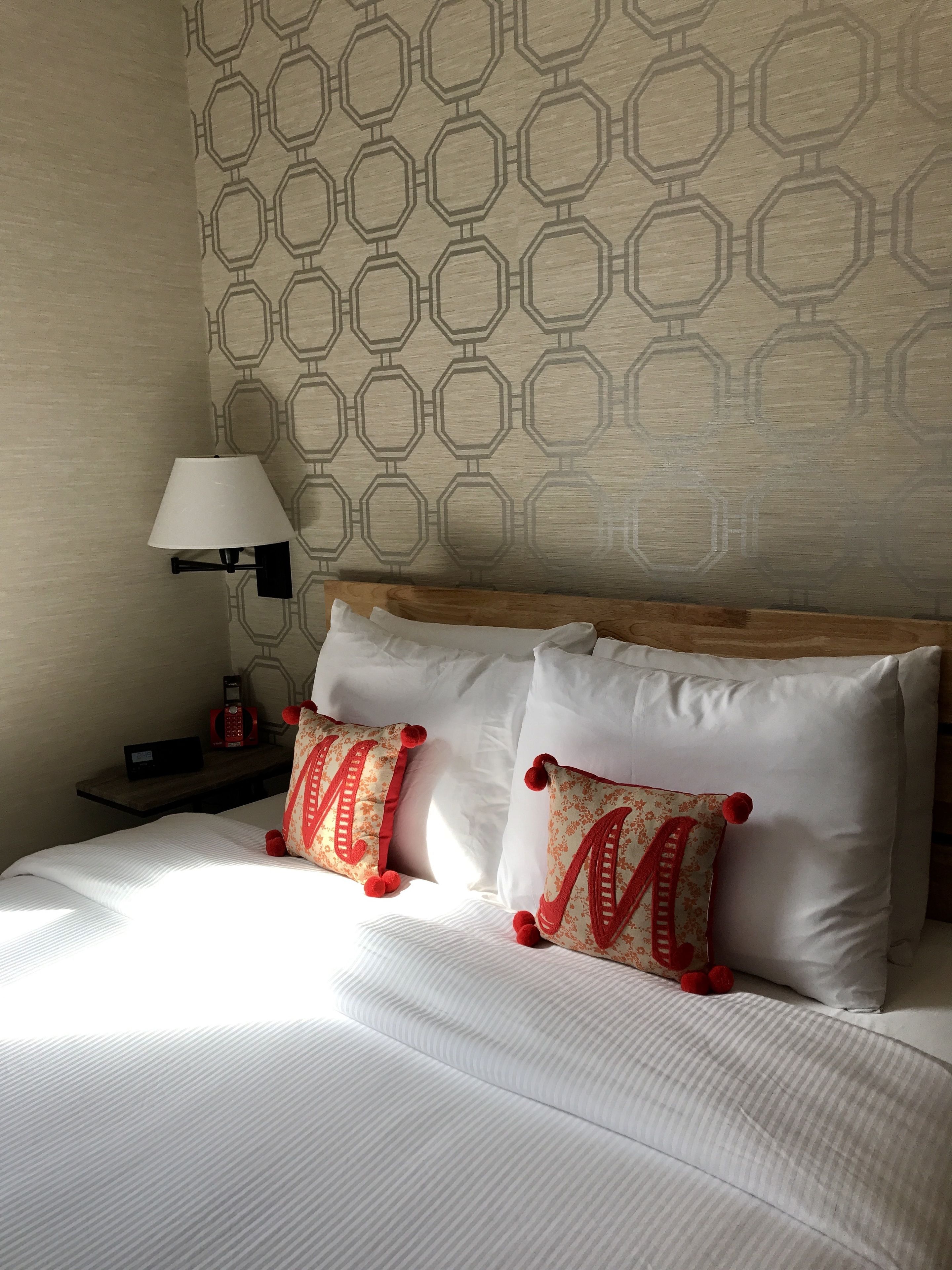 A neatly made bed with white bedding and two decorative pillows with red accents.