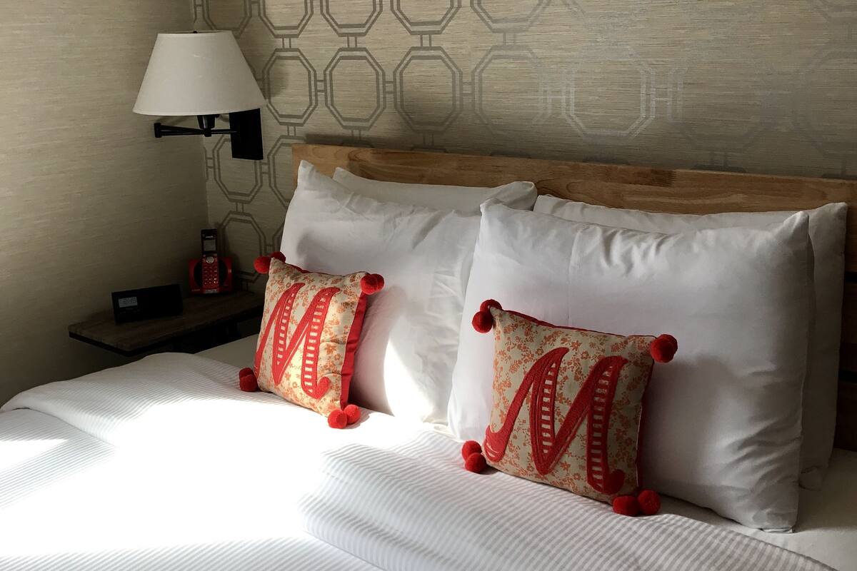 A neatly made bed with white bedding and two decorative pillows with red accents.