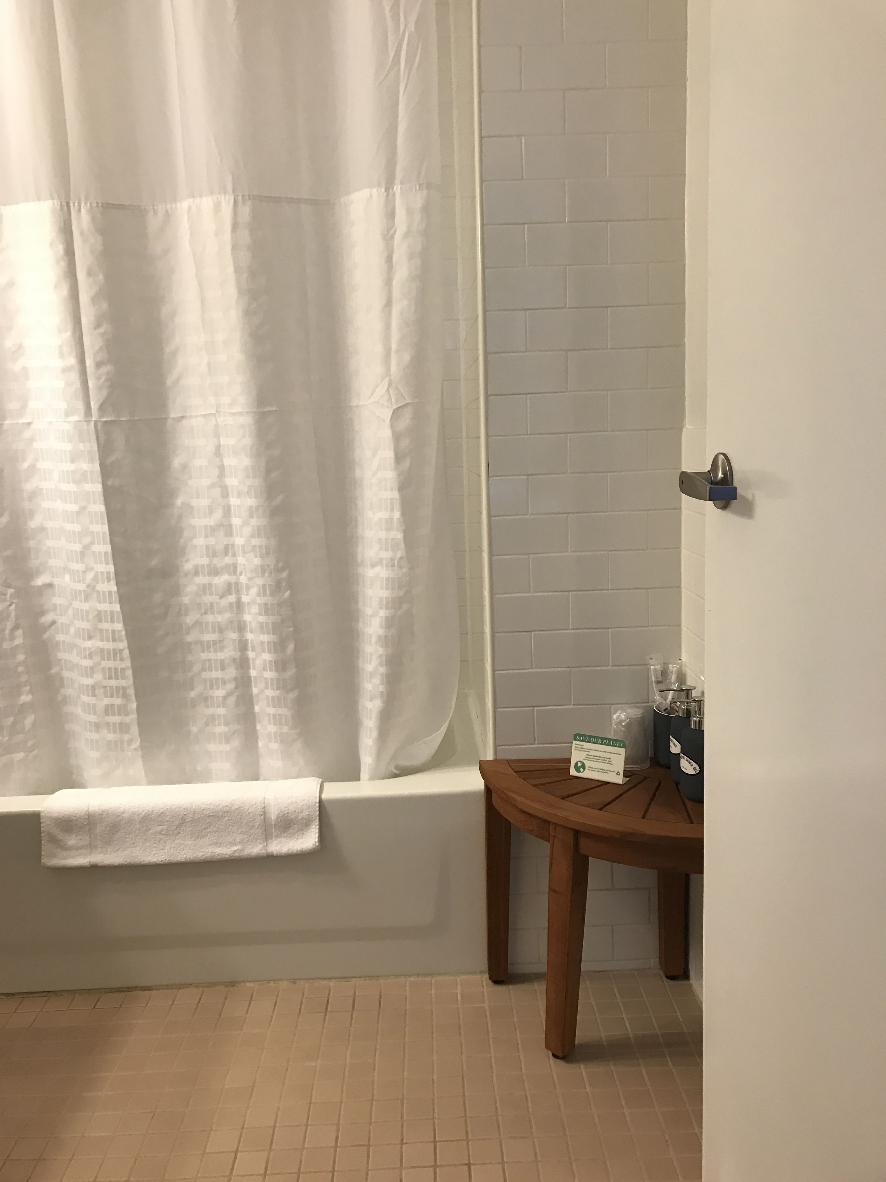 Une salle de bain avec une baignoire, un rideau de douche, un banc en bois et un panneau accroché au mur.