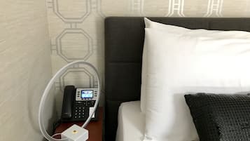 A hotel room with a bed, a bedside table with a phone and a charging station, and a patterned wall.