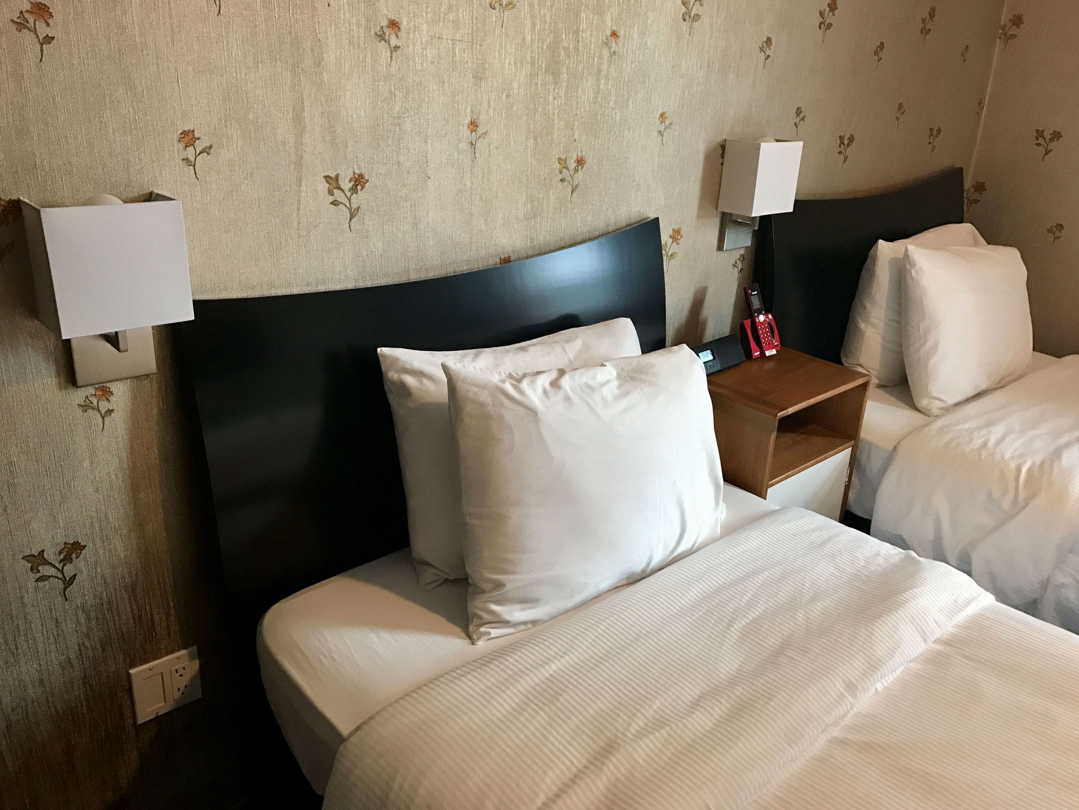 A hotel room with a large bed, two bedside tables, a nightstand, and a wall-mounted telephone.