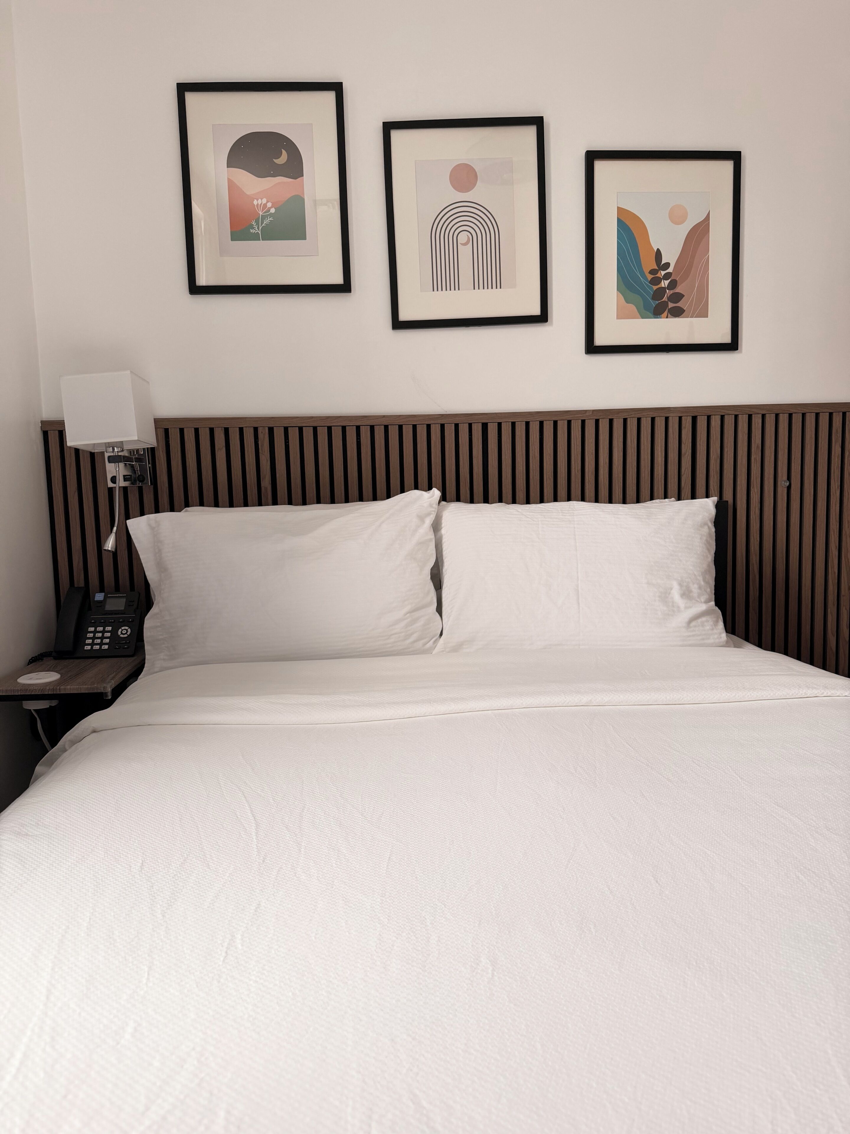 Una camera d'albergo con un letto, un comodino con un telefono e tre opere d'arte incorniciate appese al muro.