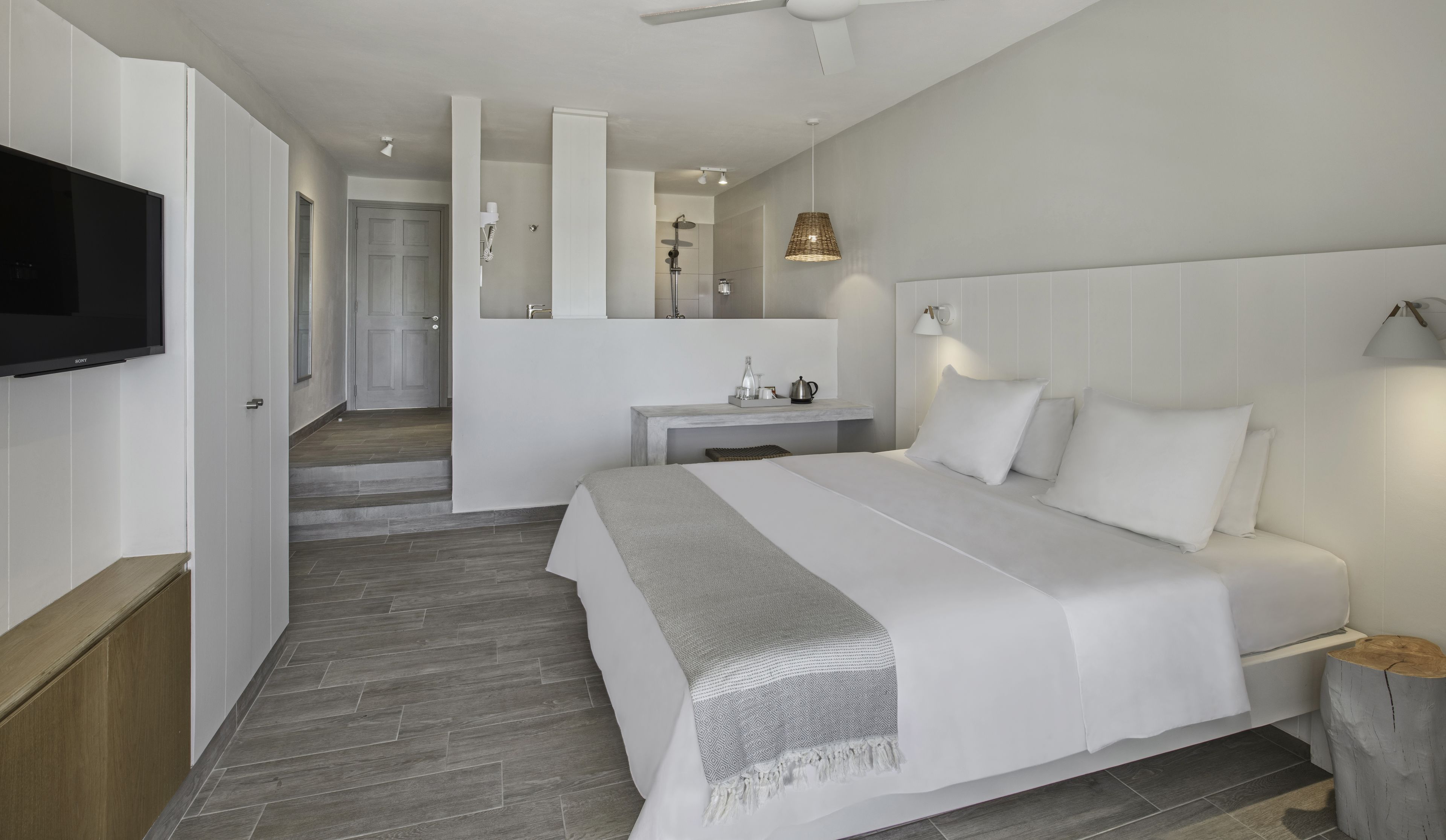 Habitación de hotel moderna con una cama grande, un televisor de pantalla plana, un escritorio y un baño con ducha.