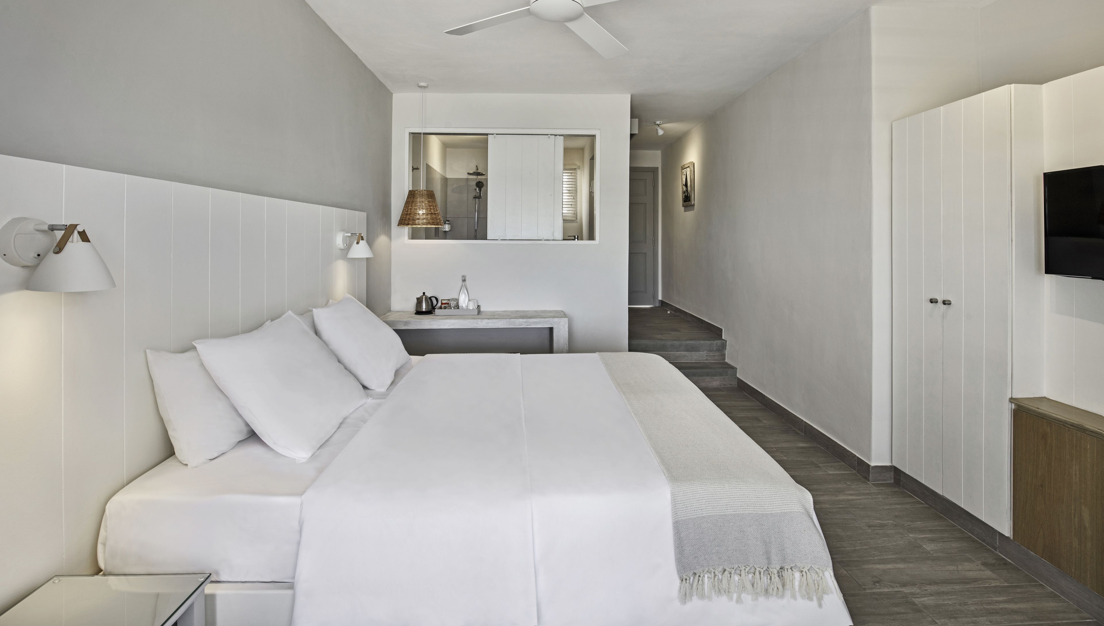 Une chambre d’hôtel moderne avec un grand lit, une table de chevet, une lampe, un miroir et un téléviseur fixé au mur.