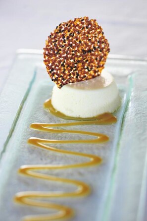 A dessert with a spherical topping on a white base, drizzled with caramel sauce. - The Bay (Black River)