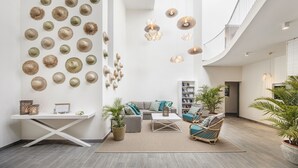 A spacious living area with a high ceiling, a white sofa, a coffee table, and a bookshelf. There are several potted plants and a wall adorned with hats. - The Bay (Black River)