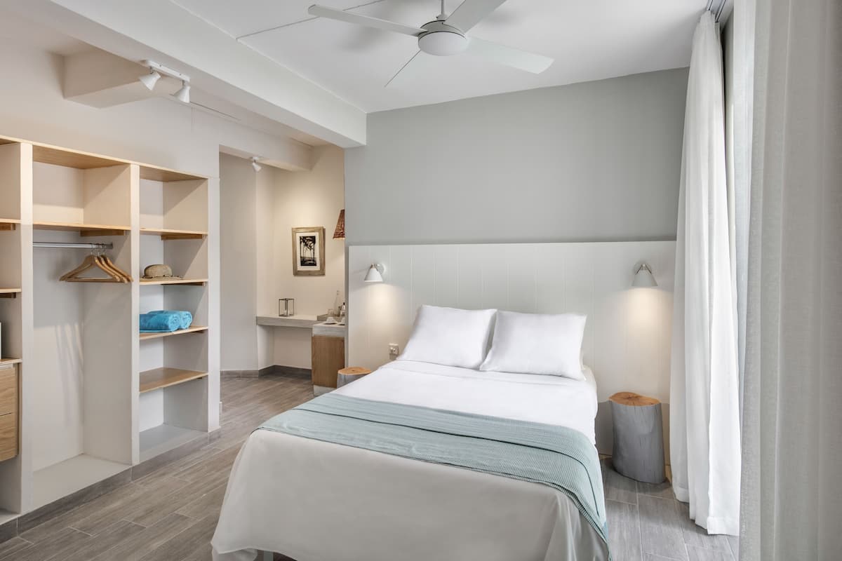 A modern hotel room with a large bed, built-in wardrobe, bedside lamps, and a ceiling fan.