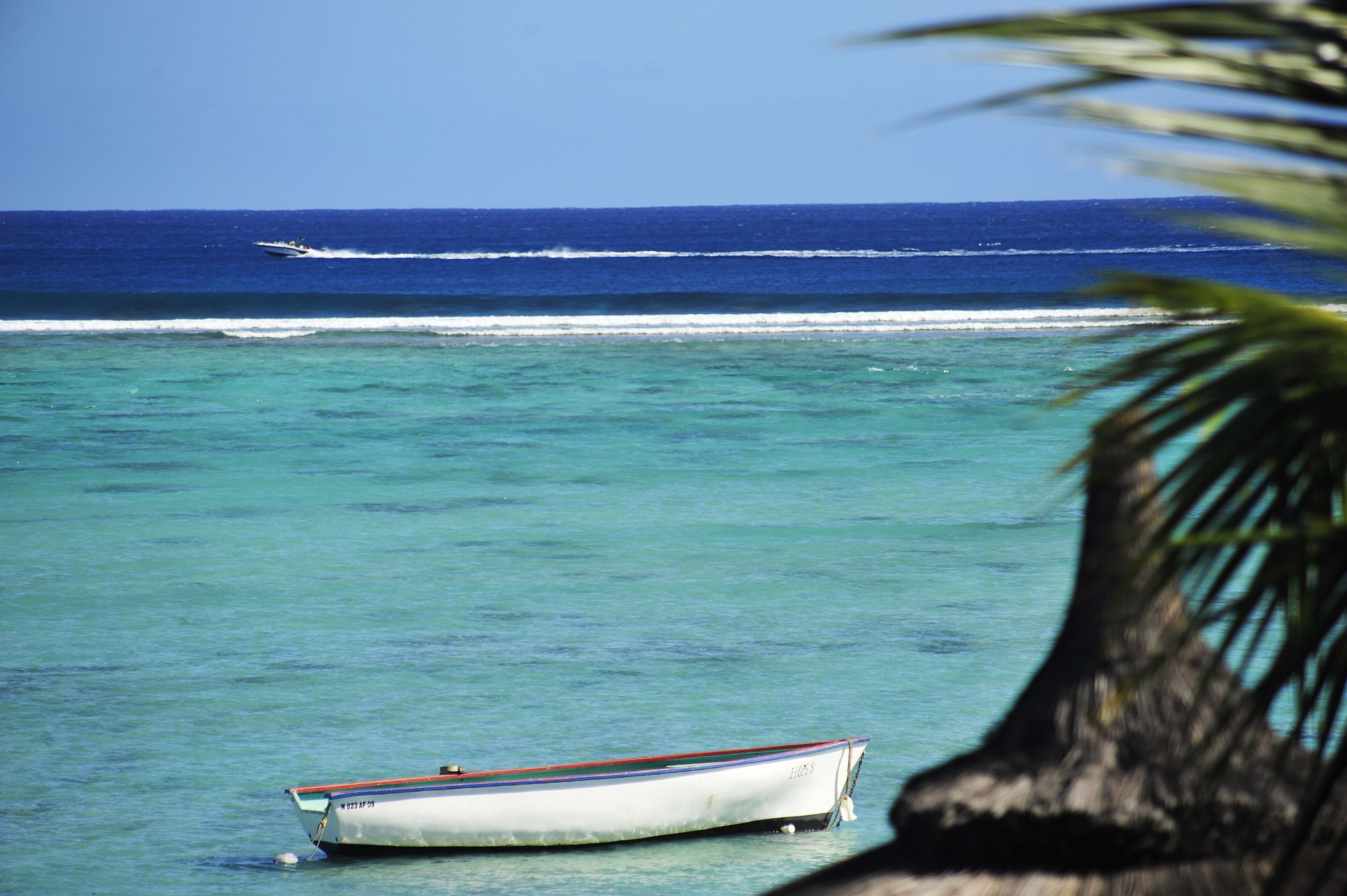 A boat anchored near the shore with clear turquoise water and a calm sea.