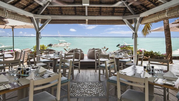 An outdoor dining area with tables and chairs, a thatched roof, and a view of the ocean. - The Bay (Black River)