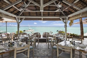 An outdoor dining area with tables and chairs, a thatched roof, and a view of the ocean. - The Bay (Black River)