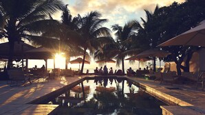 A pool area with lounge chairs and umbrellas, surrounded by palm trees, during sunset. - The Bay (Black River)