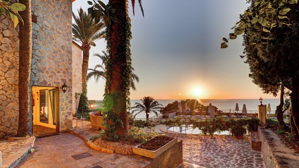 Un sendero de piedra que conduce a la entrada de un edificio, con vista al atardecer sobre el mar.
