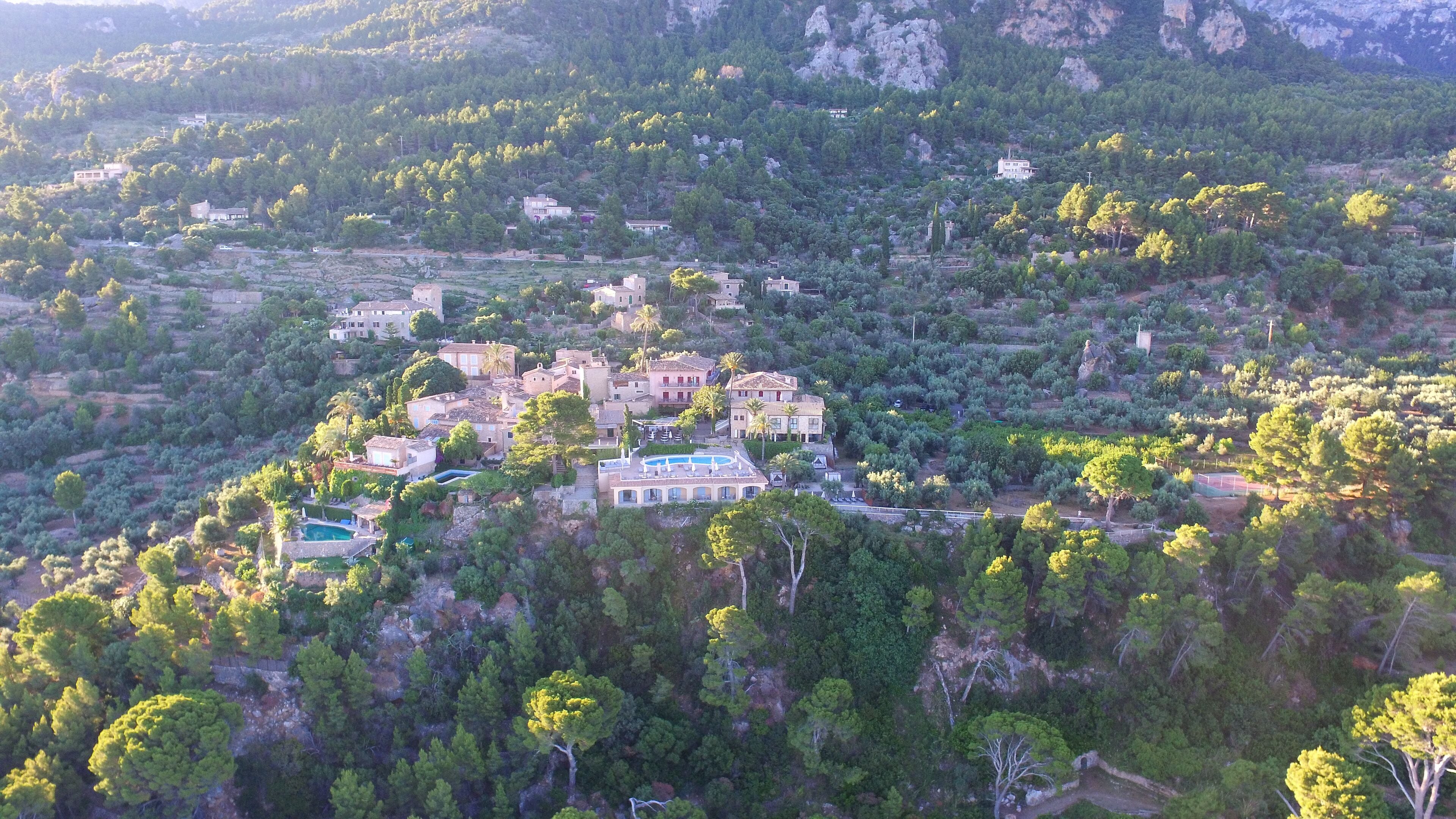 A cluster of Mediterranean-style villas surrounded by dense pine forests, with terraced gardens and a swimming pool.