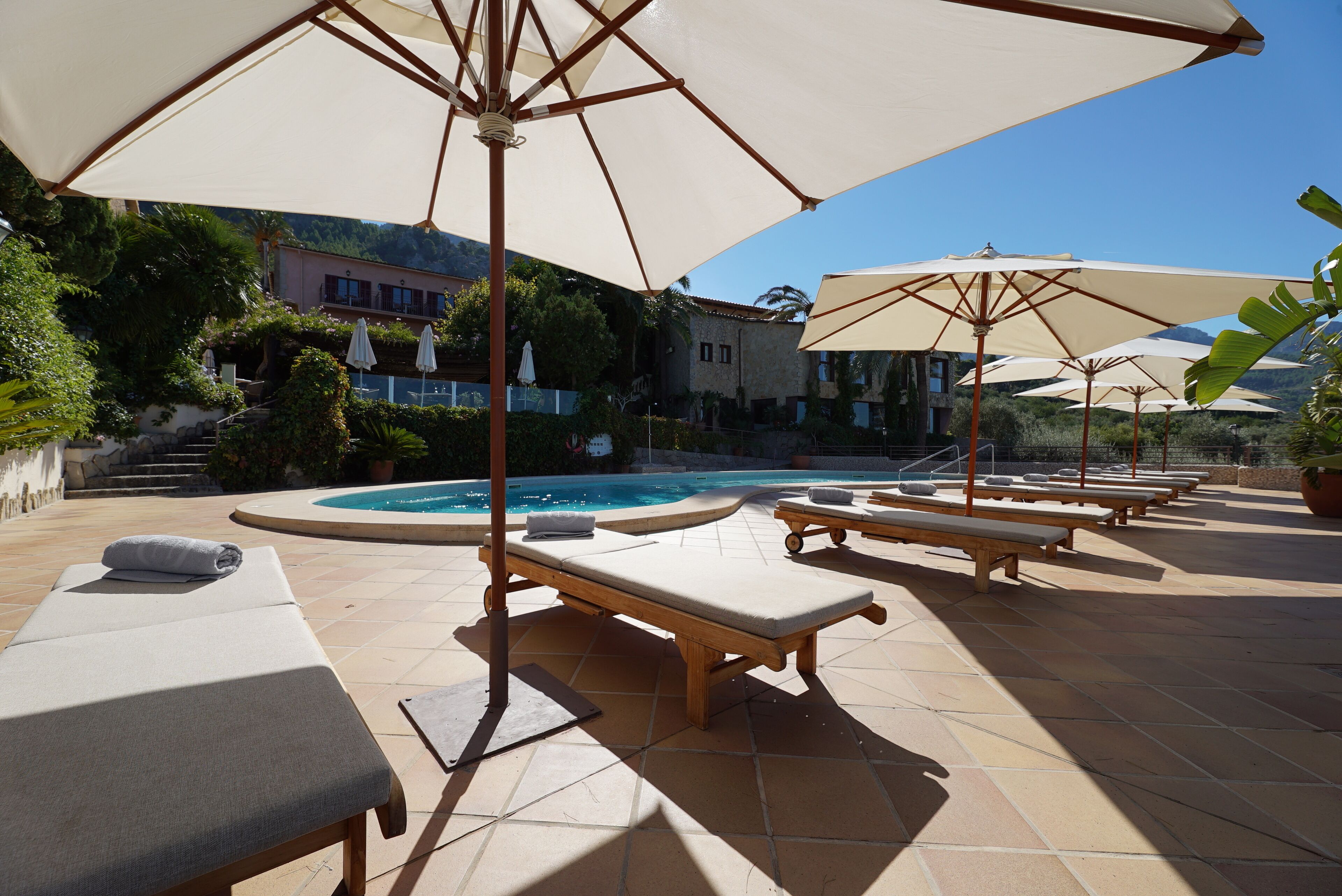 Zona junto a la piscina con sillones de descanso y sombrillas, una piscina y un edificio al fondo.