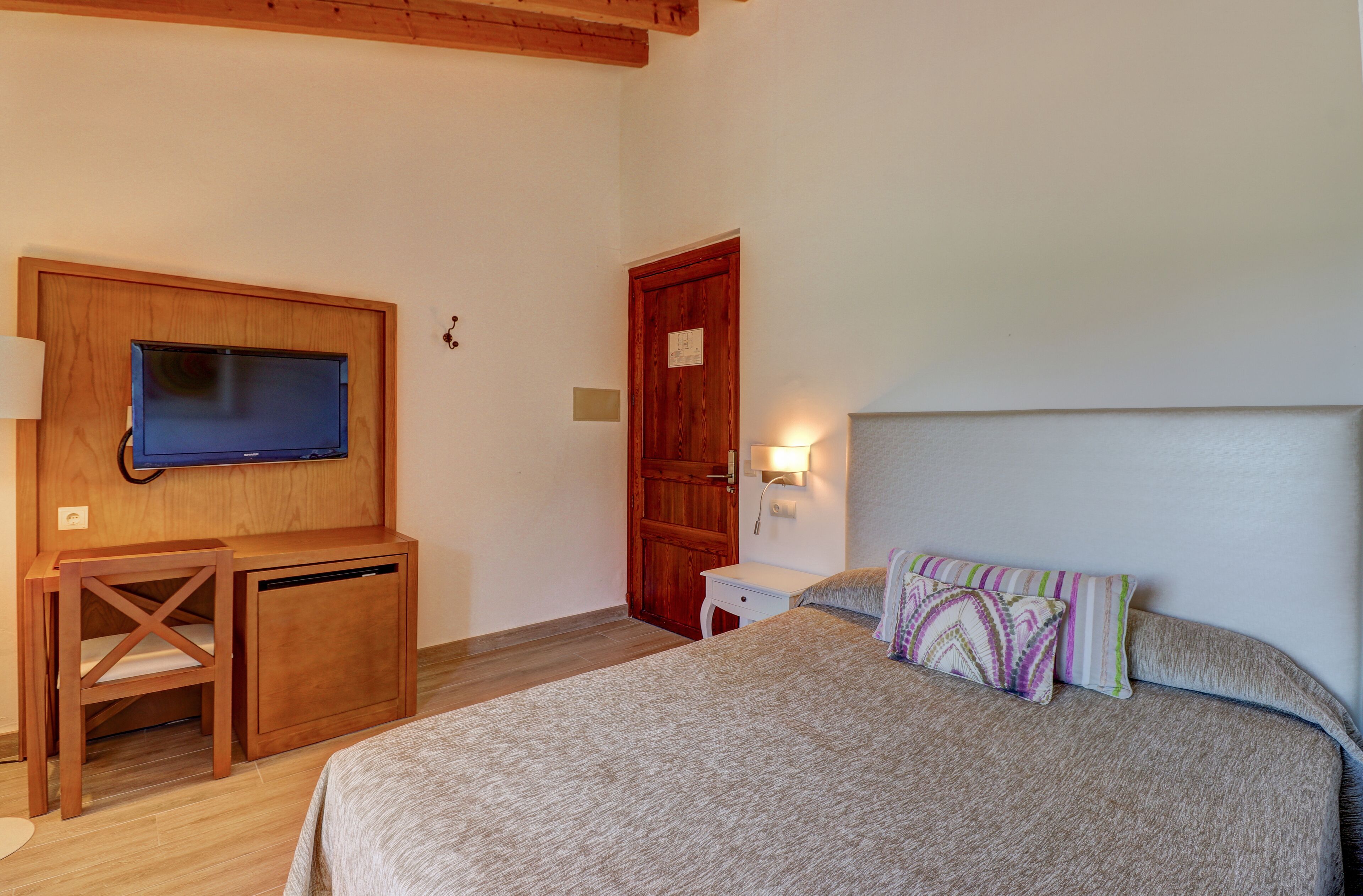 Un dormitorio con cama, escritorio, silla, televisor y puerta.