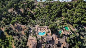 Vista aérea de una propiedad costera con abundante vegetación, una piscina central y varias piscinas más pequeñas.