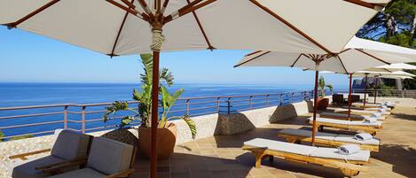 A terrace with lounge chairs and umbrellas overlooking the sea.