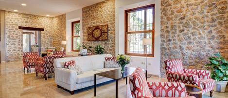 Amplia sala de estar con pared de piedra, un sofá blanco, sillones estampados y una mesa de centro.