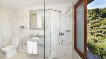 A bathroom with a marble wall, a toilet, a sink, a shower, and a large mirror.
