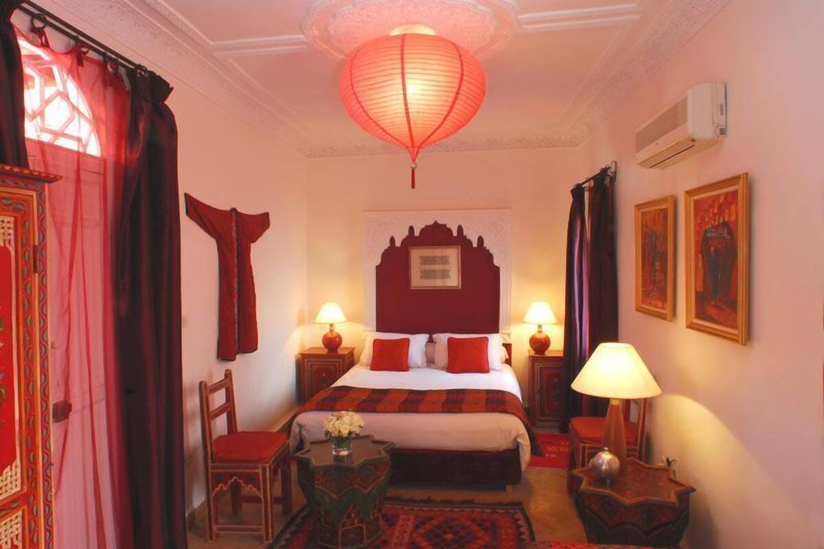 A hotel room with a large bed, two bedside lamps, a red lantern, a small table with a vase, and a chair.