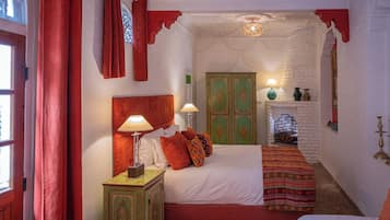 A traditional room with a bed, a nightstand, a green cabinet, and a fireplace.