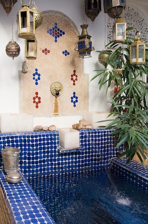 Ein marokkanisch gestaltetes Bad mit blauen Mosaikfliesen, hängenden Laternen und einer Zierwand.