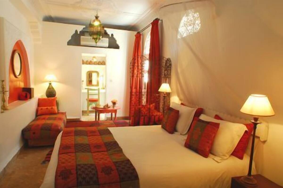 A hotel room with a large bed, two bedside tables, a nightstand, a mirror, and a hanging light fixture.