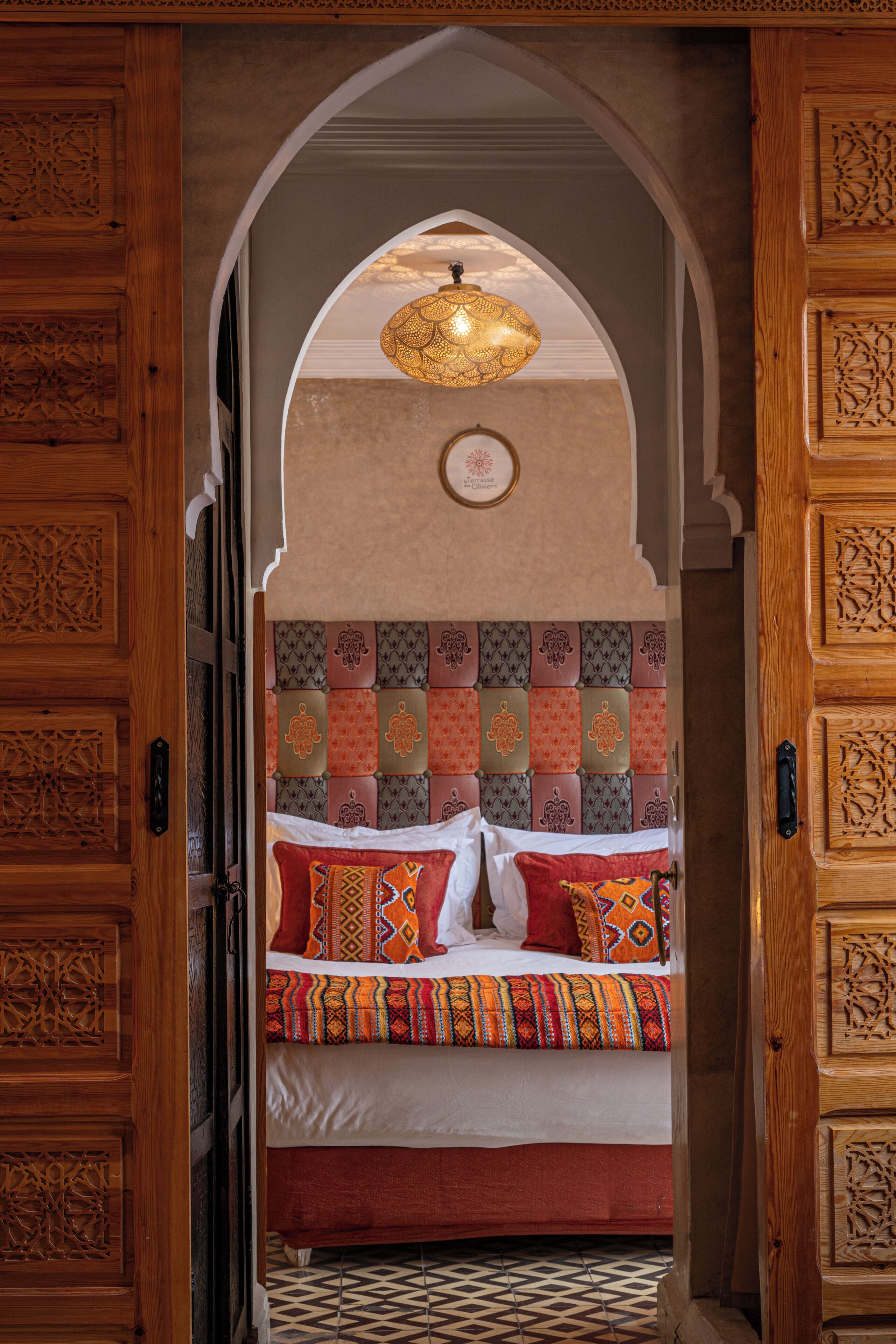 A traditional room with a bed, ornate wooden doors, and a decorative ceiling light.