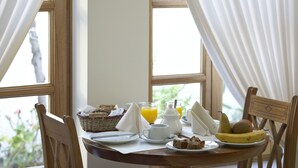 A breakfast table with a basket, juice, a teapot, a plate with a slice of cake, a banana, and a pear.