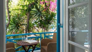 A balcony with wicker chairs, a small round table, and a view of lush greenery and pink flowers.