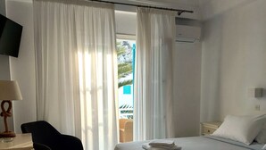 A hotel room with a bed, a chair, a desk with a lamp, and a television on the wall.