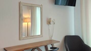 Una camera d'albergo con una scrivania in legno, una sedia nera, una TV a parete e uno specchio.