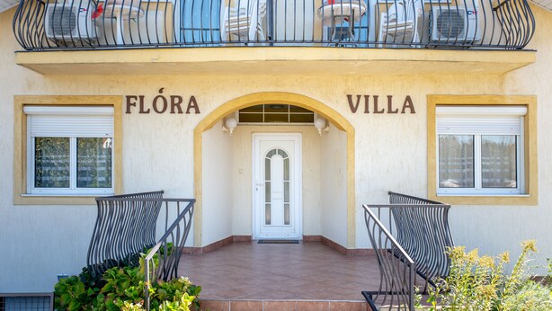 Um edifício com varanda, uma porta e duas cadeiras na frente.