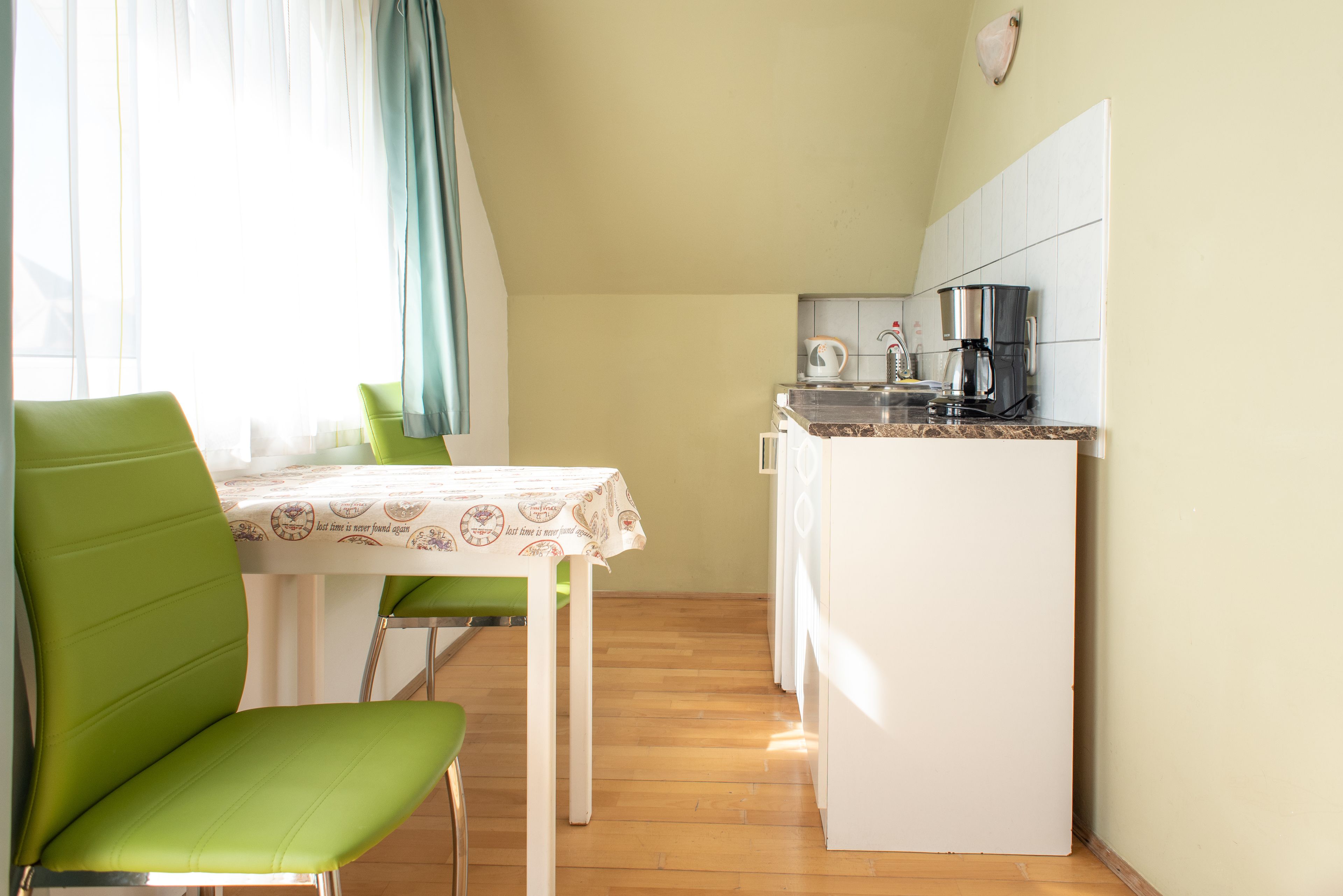Una kitchenette pequeña con refrigerador, cafetera y ventana con cortinas.