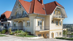 Uma casa de dois andares com telhado de telhas vermelhas, varandas e um jardim.