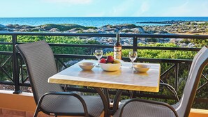 Uma mesa com uma garrafa, tigelas e frutas numa varanda com vista para o oceano.