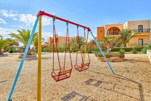Un parque infantil con columpios y un edificio al fondo.