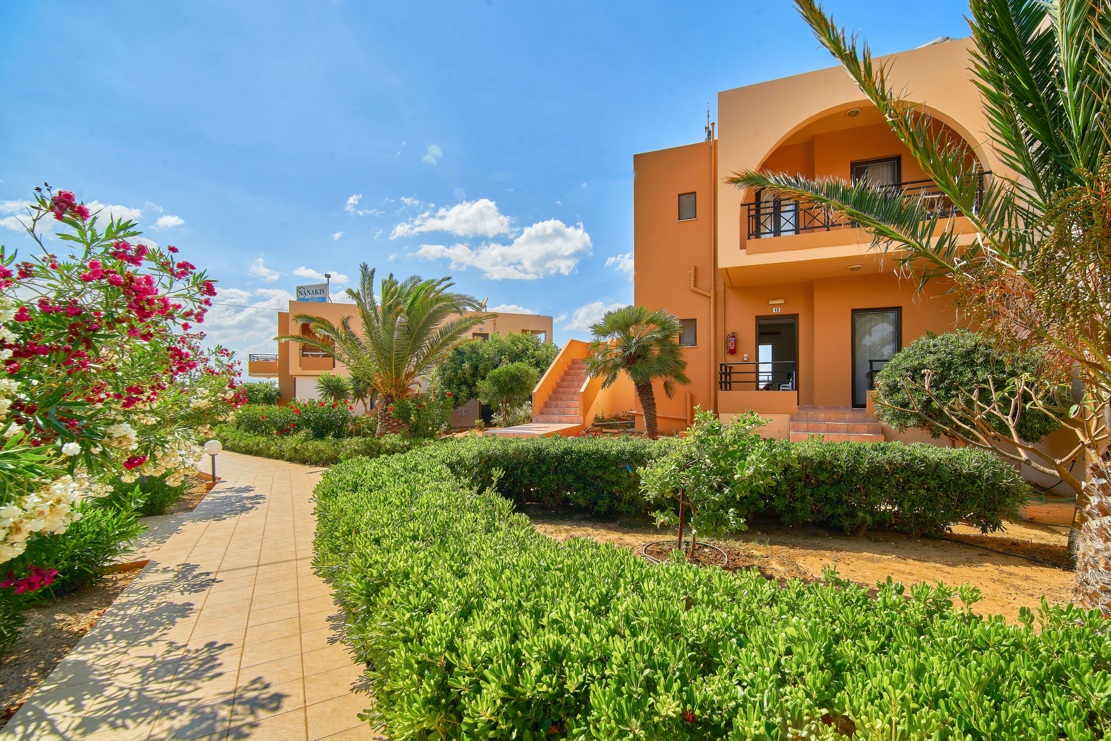 A hotel with a paved walkway, well-maintained greenery, and a clear blue sky.