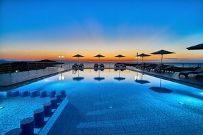 A poolside area with lounge chairs and umbrellas, a tiled pool, and a sunset view. - Nanakis Beach Apartments (Chania)