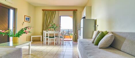 A modern living room with a sofa, a glass coffee table, a dining table with chairs, and a balcony with curtains.