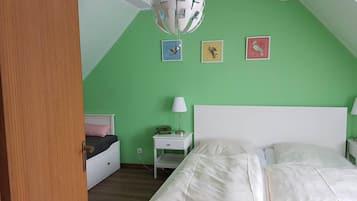 Un dormitorio con una pared verde, una cama blanca, una mesita de noche con lámpara y un ventilador de techo.