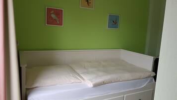 Ein Einzelbett mit weißer Matratze und Kissen in einem Zimmer mit grünen Wänden.