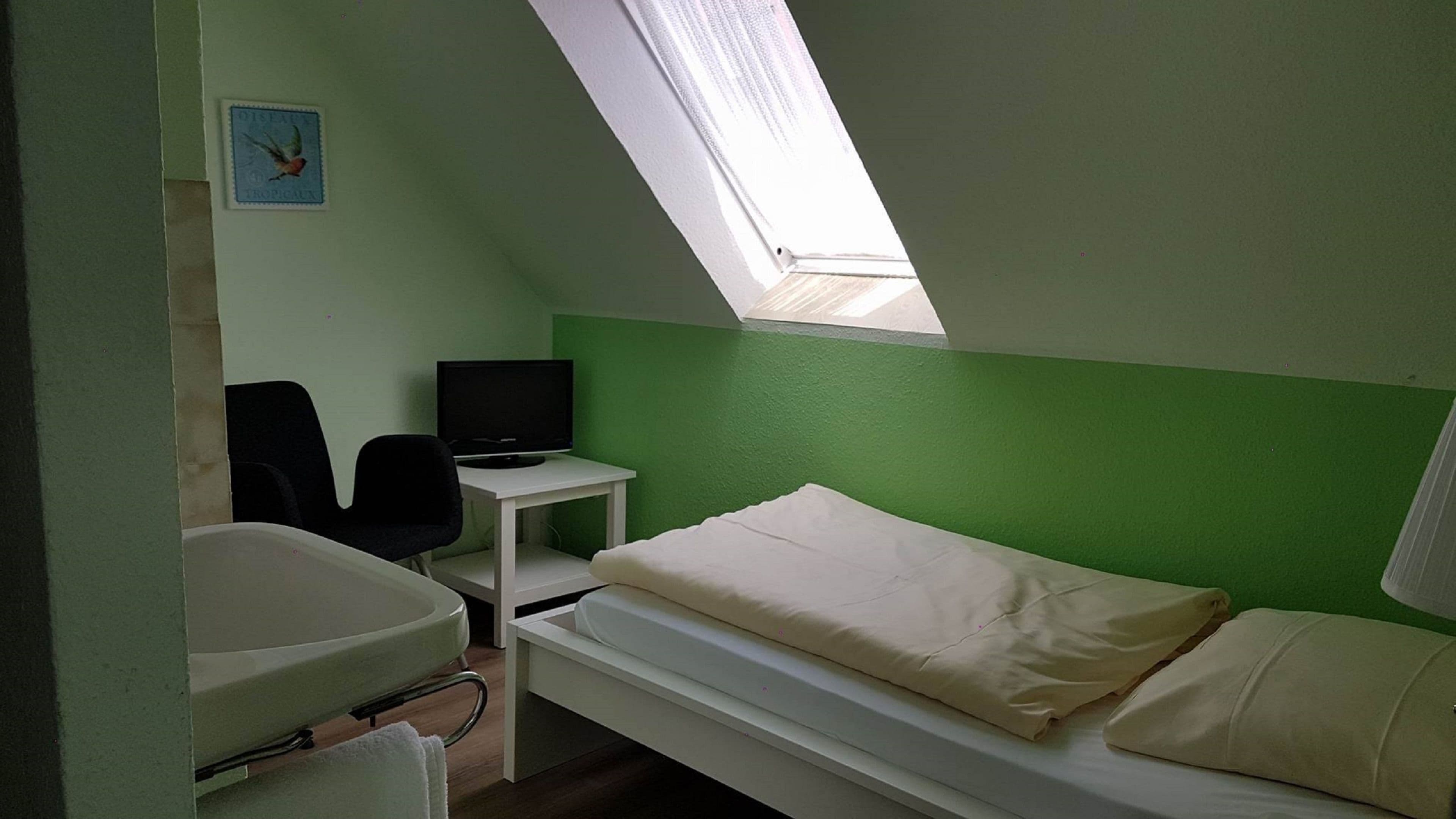 Un petit logement composé d’une seule pièce, comprenant un lit, un bureau avec un ordinateur, une chaise et une fenêtre.