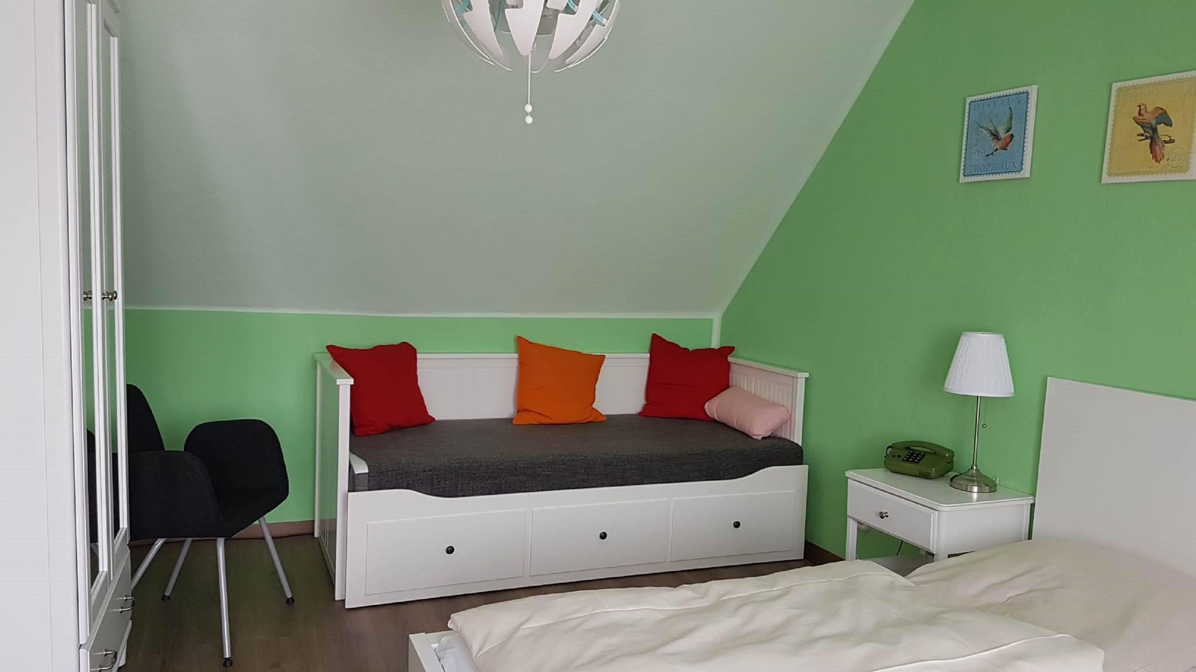 A bedroom with a bed, a chair, a nightstand, and a lamp.