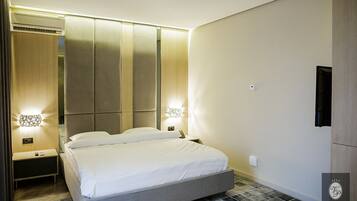 A modern hotel room with a large bed, two bedside tables, a wall-mounted TV, and a built-in wardrobe.