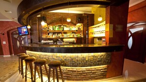 A bar area with a stone wall, wooden stools, and a television screen. - VisPas Hotel (Chisinau)