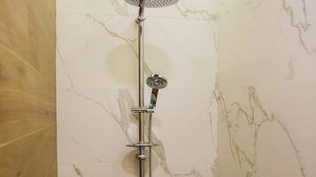 A shower with a handheld showerhead and a handheld faucet, set against marble walls.